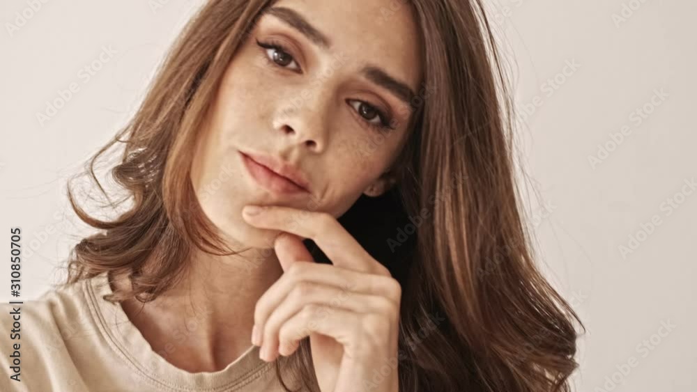 Close up view of Mystery beauty brunette woman posing with finger near the lips and looking around over grey background Close up view of Mystery beauty brunette woman posing with finger near the lips and looking around over grey background