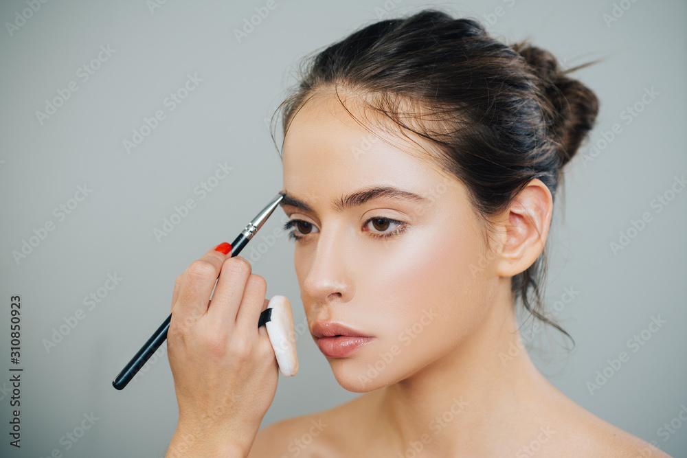 Beautiful young woman getting eyebrow make-up. The artist is applying eyeshadow on her eyebrow with brush. Young model girl getting her natural eyebrow makeup.