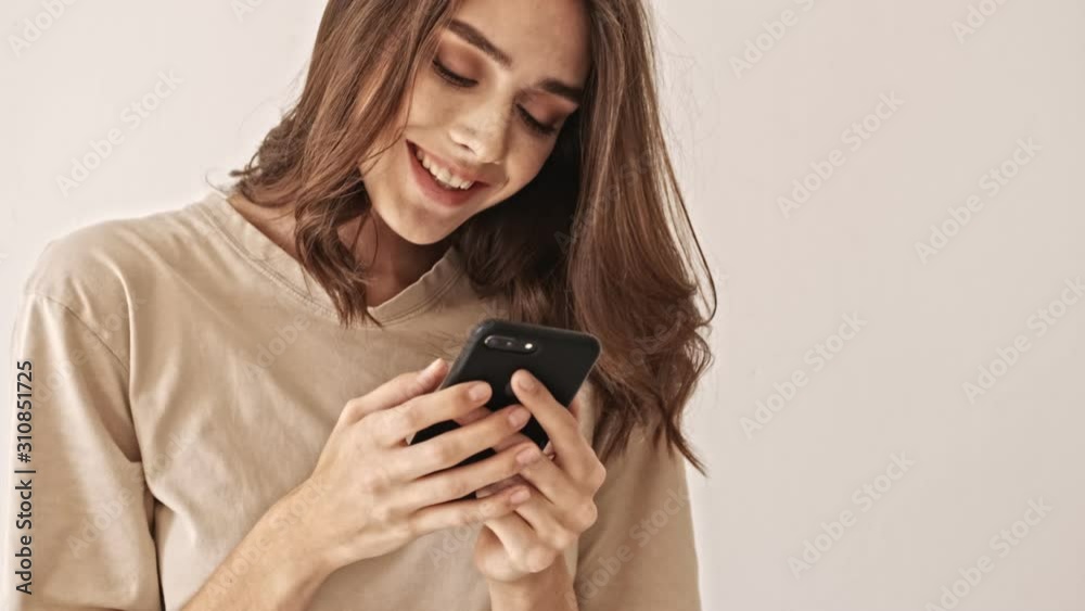Smiling beauty brunette woman using smartphone and enjoying this moment over grey background Smiling beauty brunette woman using smartphone and enjoying this moment over grey background