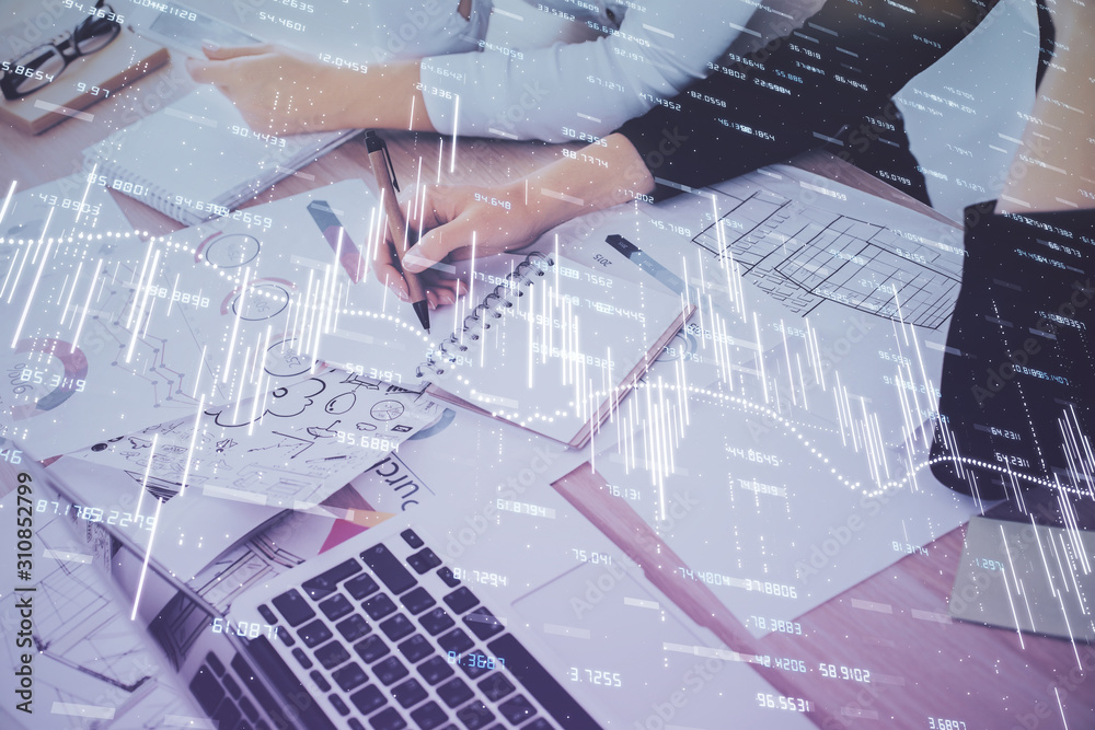 A woman hands writing information about stock market in notepad. Forex chart holograms in front. Concept of research. Double exposure