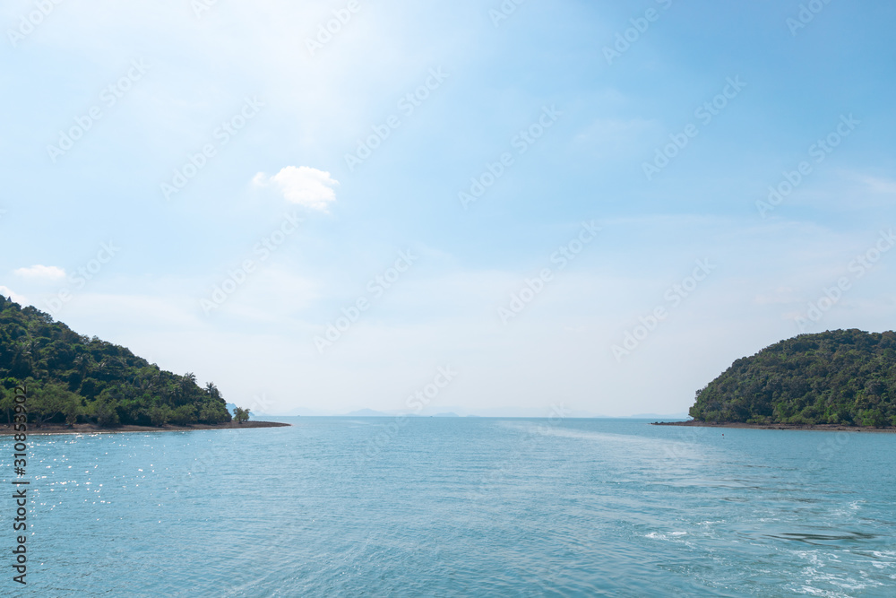 Ocean with soft blue sea water in sunny day between two small island full of forest at there