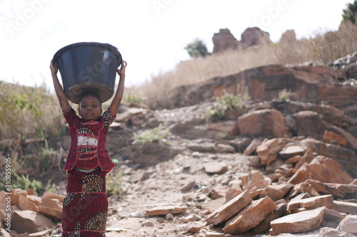 Landscape shot of African Black Schoolgirl Walking with Heavy Water Bucket