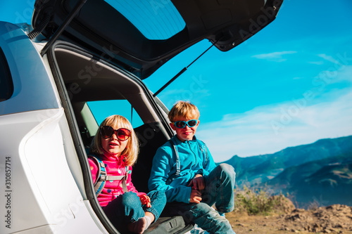 happy kids- boy and girl- travel by car in mountains