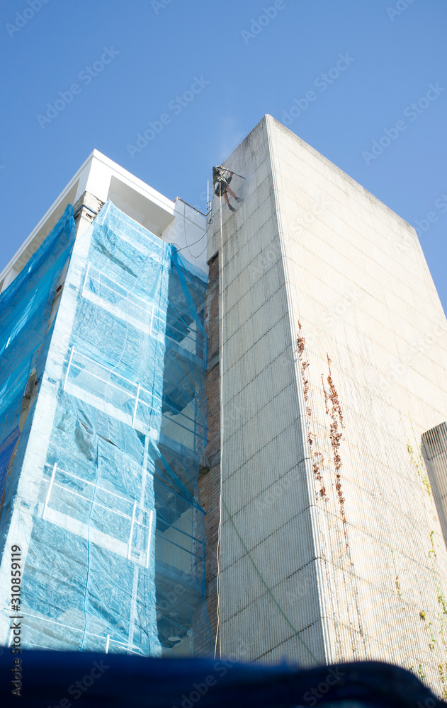 Rope access technician washing building facade Rope access technician washing building facade