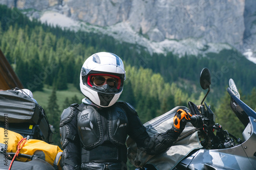 Close up of girl dressed in protective suit of body armor, tutle prtotective jacket, with helmet and glowes. Adventure motorcycle and mountains on background. Outdoors.