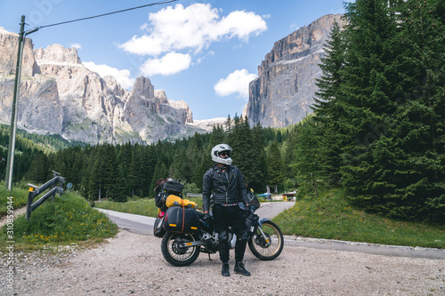 Motorcyclist man standing with adventure motorbike on the mountain road, beautiful summer view, danger road in mountains, freedom, extreme vacation. Sella Towers. Passo Pordoi, Italy