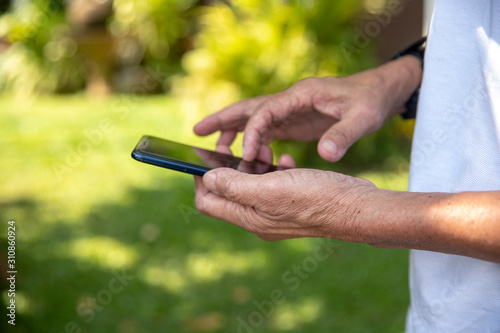 Hands of an elderly man holding and using a phone. The concept of teaching new technologies to older people, communication with the older generation. Image.