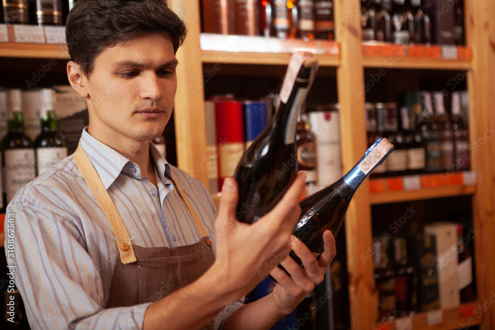 Young male winemaker working at his shop, holding two wine bottles, copy space