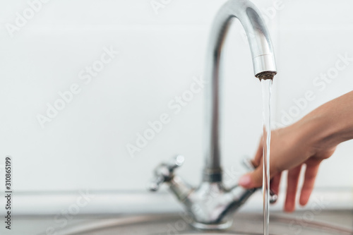 woman hand opening silver faucet or water tap with metal washing sink in the kitchen 