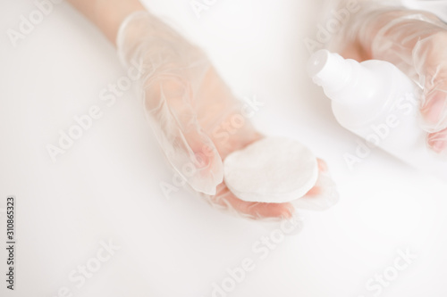 Womans manicurist hand in medical gloves. holding a bottle with lotion or acetone, apllying on cotton pad