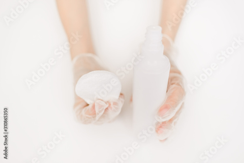 Womans manicurist hand in medical gloves. holding a bottle with lotion or acetone  apllying on cotton pad