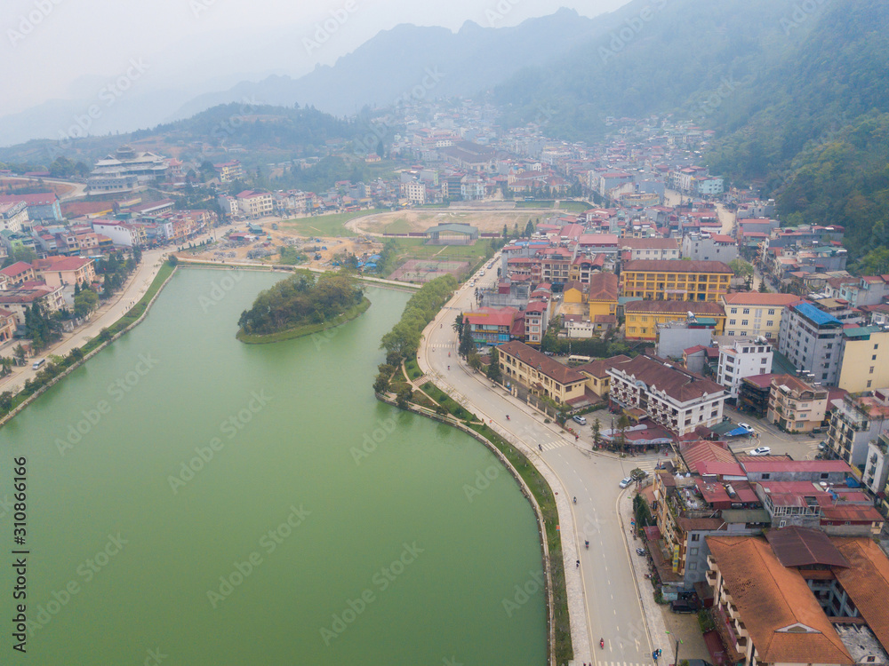 Fototapeta premium Aerial view of Sapa cityscape covered by fog with Sapa lake an iconic emerald green lake in the downtown of Sapa the capital city in Lao Cai province in north-west of Vietnam.