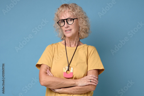 Beautiful mature blonde woman in eyeglasses and yellow shirt is looking at camera and smiling with folded hands. Studio shot photo