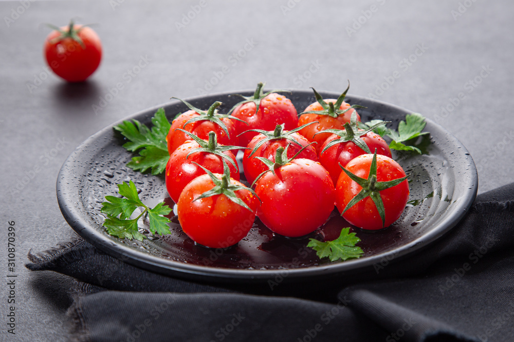 Fresh cherry tomatoes on black round plate,  on dark background.