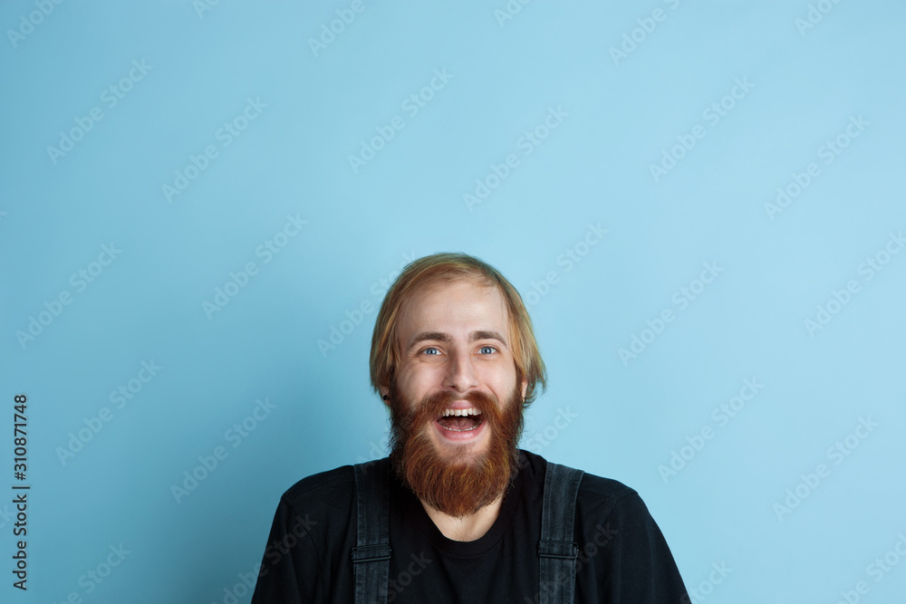 Obraz premium Portrait of young caucasian man looks dreamful, cute and happy. Looking up and thinking on blue studio background. Copyspace for your advertising. Concept of future, target, dreams, visualisation.
