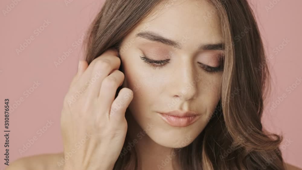 A close-up view of young calm beautiful woman is opening her eyes and looking to the camera isolated over pink background A close-up view of young calm beautiful woman is opening her eyes and looking to the camera isolated over pink background