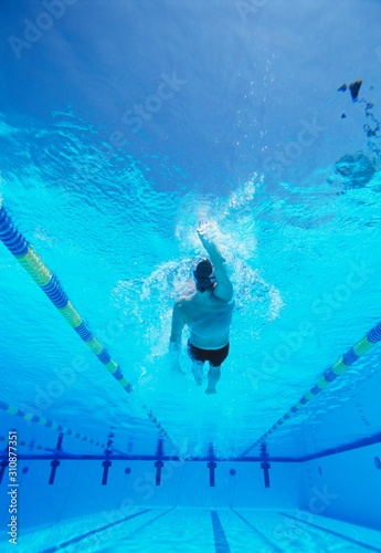 Underwater shot of young male athlete doing backstroke in swimming pool photo