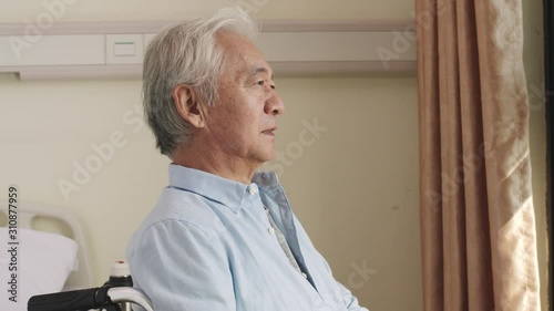 senior asian man sitting in wheel chair by the window turning to camera smiling