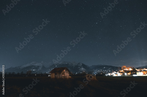 Wooden Hut With Snow Mountains In The Background At Night Time.