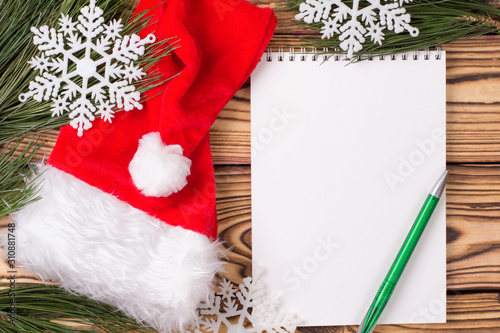 Christmas background with blank notebook, pine branches, santa hat and Christmas toys on wooden table. Copy space. Flat lay