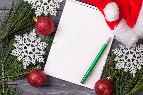 Christmas background with blank notebook, pine branches, santa hat and Christmas toys on wooden table. Copy space. Flat lay