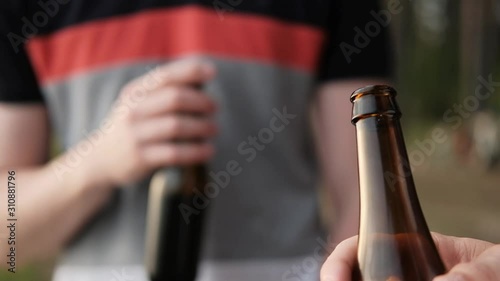 Two young men drink beer from bottles and relax outdoors. A weekend in nature, a meeting of friends and party in the woods.