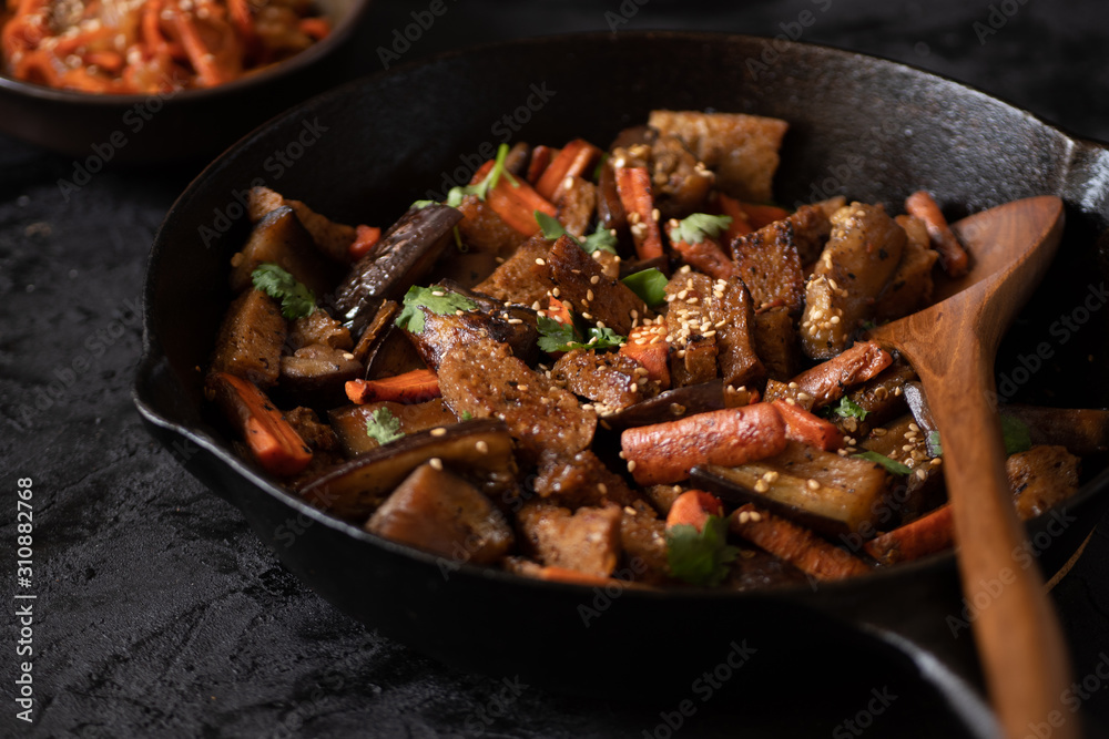 Vegan Korean seitan, carrot and eggplant fry over rice with kimchi in a black bowl