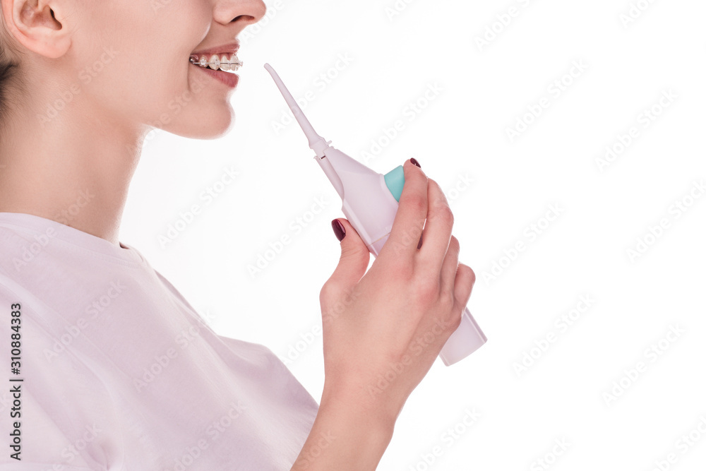 Side view of young positive woman with braces on teeth. Hold oral water irrigator in hand. Ready to clean teeth. Oral dental care. Cut view. Isolated young woman on picture. Side view of young positive woman with braces on teeth. Hold oral water irrigator in hand. Ready to clean teeth. Oral dental care. Cut view. Isolated young woman on picture.