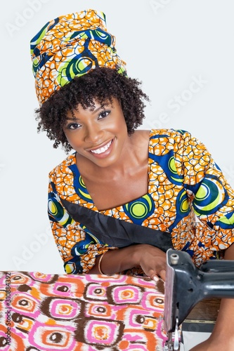 Portrait of an African American female fashion designer sewing fabric over gray background
