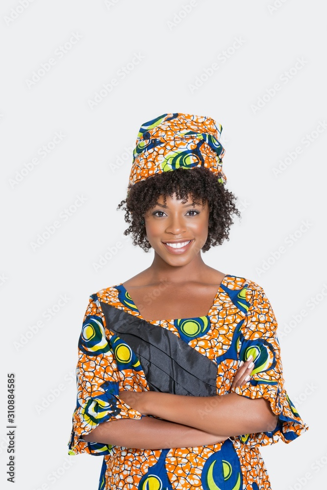 Portrait of young woman in African print attire standing arms crossed over gray background Portrait of young woman in African print attire standing arms crossed over gray background