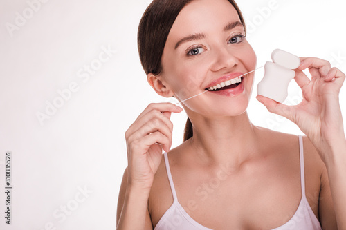 Cheerful happy young woman posing on camera and smile. Hold dental floss with white box and show it. Oral care. Dental health. Isolated over white background.