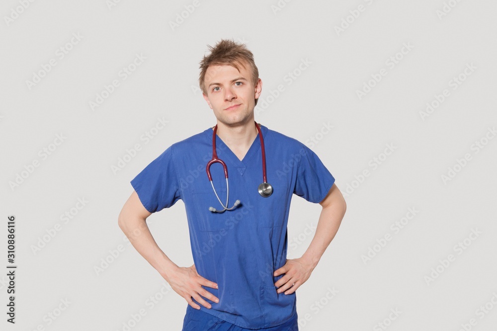 Portrait of male surgeon standing with hands on hips over gray background