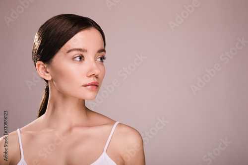 Serious concentrated calm and peaceful young woman look to right. Side view. Natural beauty and fantastic look. Healthy glowing skin with no acne or spots. Skin care. Isolated over beige background.