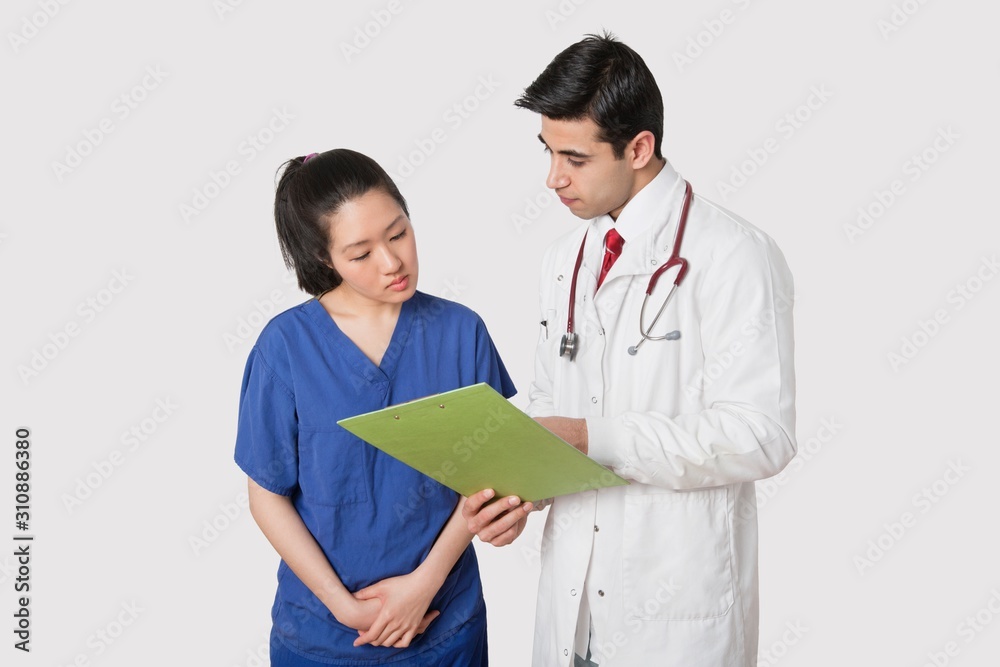 Doctor discussing medical report with female nurse over gray background Doctor discussing medical report with female nurse over gray background
