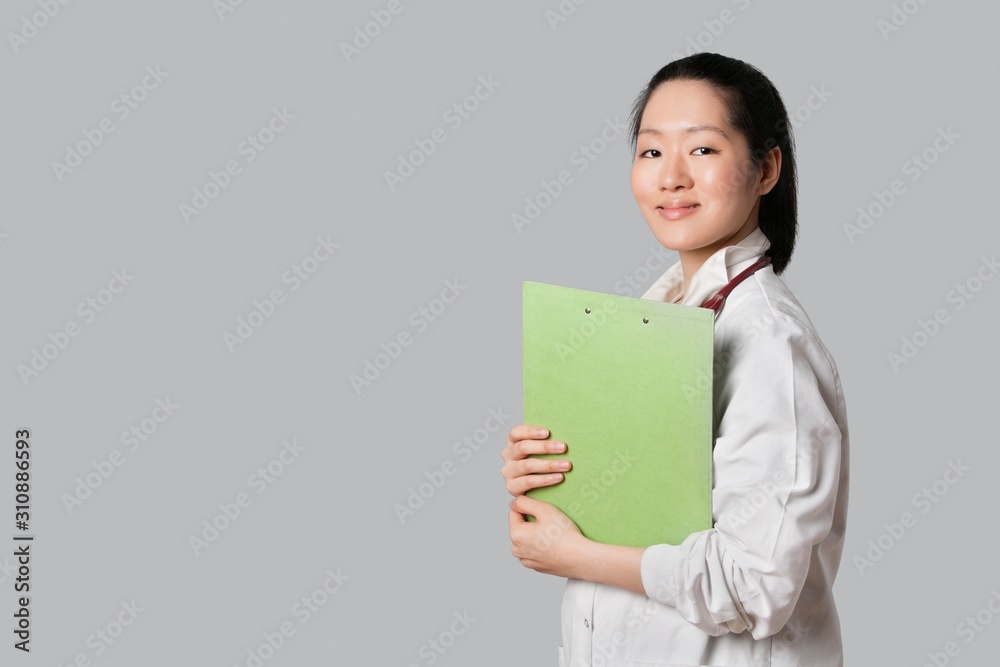 Portrait of a confident Asian female doctor holding clipboard over gray background Portrait of a confident Asian female doctor holding clipboard over gray background