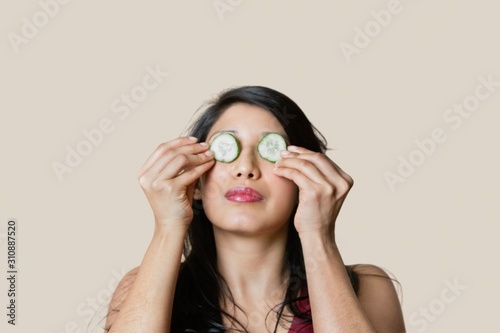 Young woman placing cucumber on eyes over colored background