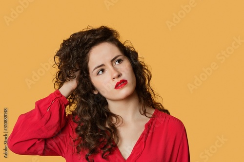 Thoughtful young woman with hand in hair over colored background