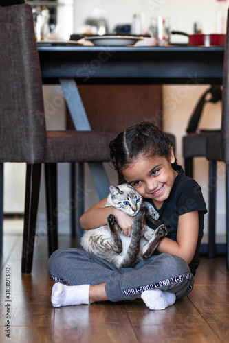 Sweet and Happy little girl child with her kitten cat on the floor in the house.  Brunette and brazilian.