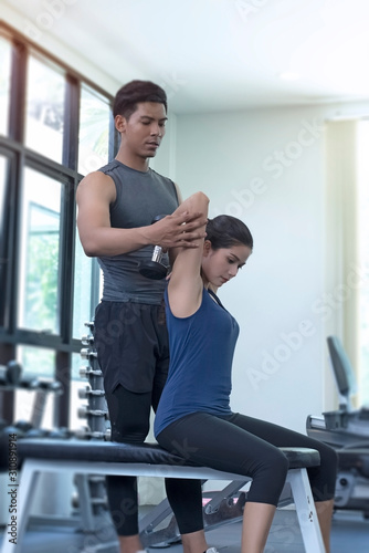The trainer teaching beautiful woman for use dumbbell,exercise program,at fitness center
