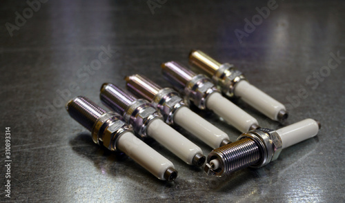 Spark plugs for a modern engine on a steel background. Six spark plugs, one in focus, the rest in the background blurred. Original spare parts for a modern car as a guarantee of quality, durability.
