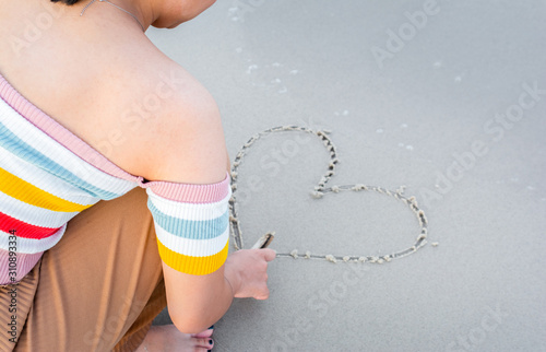 Girl draw heart picture on a beach.