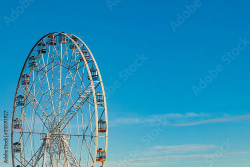 High ferris wheel with multi-colored cabins on a background of blue sky
