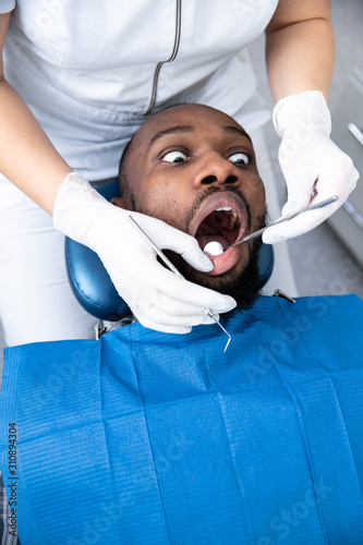Young african-american man visiting dentist s office for prevention and treatment of the oral cavity. Man and woman doctor while checkup teeth. Healthy lifestyle  healthcare and medicine concept.