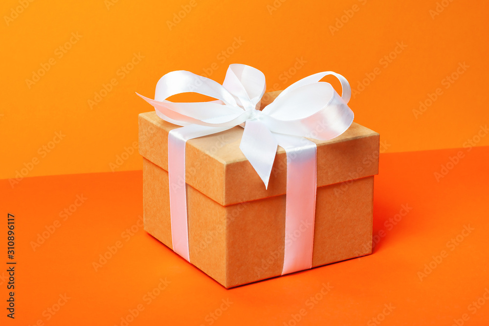 Obraz premium Trendy attractive minimalistic gift on the orange background. Merry Christmas, St. Valentine's Day, Happy Birthday and other holidays concept.