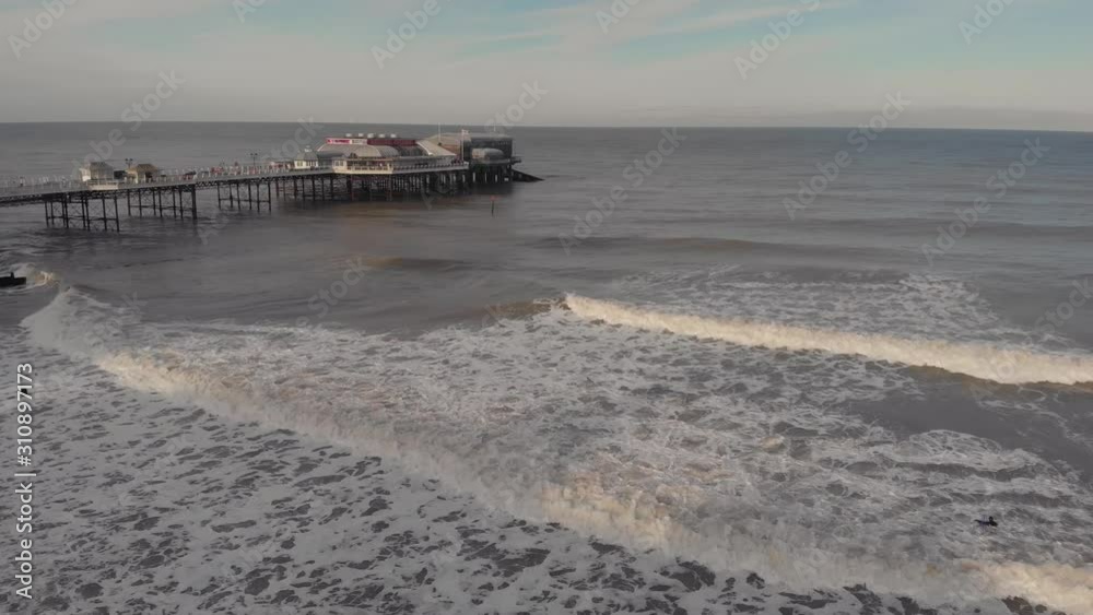 Surfers waiting to ride waves in a rough sea near a structure on which an amusement park on the sea is seen Surfers waiting to ride waves in a rough sea near a structure on which an amusement park on the sea is seen