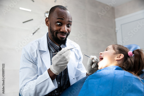 Young caucasian girl visiting dentist's office for prevention and treatment of the oral cavity. Child and african-american doctor while checkup teeth. Healthy lifestyle, healthcare and medicine