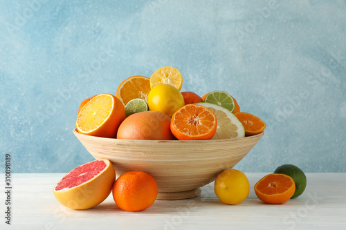 Fototapeta Naklejka Na Ścianę i Meble -  Juicy citrus fruits in bowl on wooden table against blue background, space for text