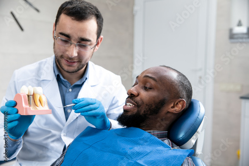 Young african-american man visiting dentist's office for prevention and treatment of the oral cavity. Man and male doctor while checkup teeth. Healthy lifestyle, healthcare and medicine concept.