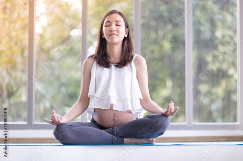 Young pregnant woman practicing yoga while sitting in lotus position at home