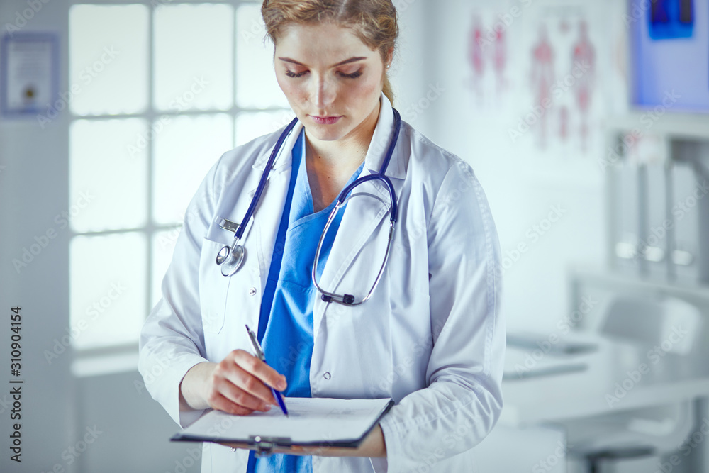 Young woman doctor is standing with board with clipboard smilin Young woman doctor is standing with board with clipboard smilin